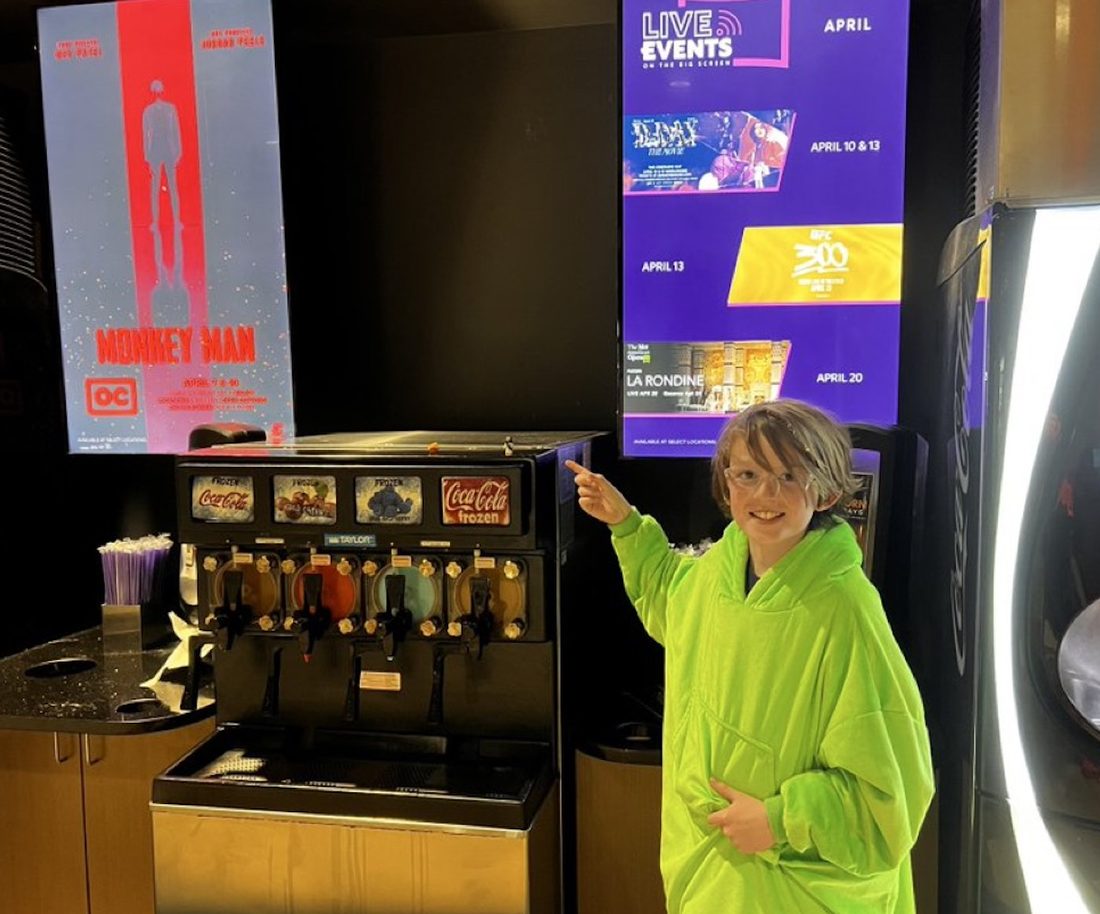 A boy pointing at a Mini Jesus figure left at a movie theater drink station